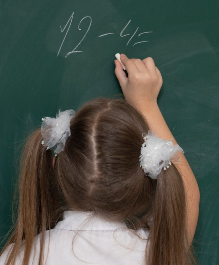 services-02 Young girl writing a subtraction problem on a chalkboard during class.