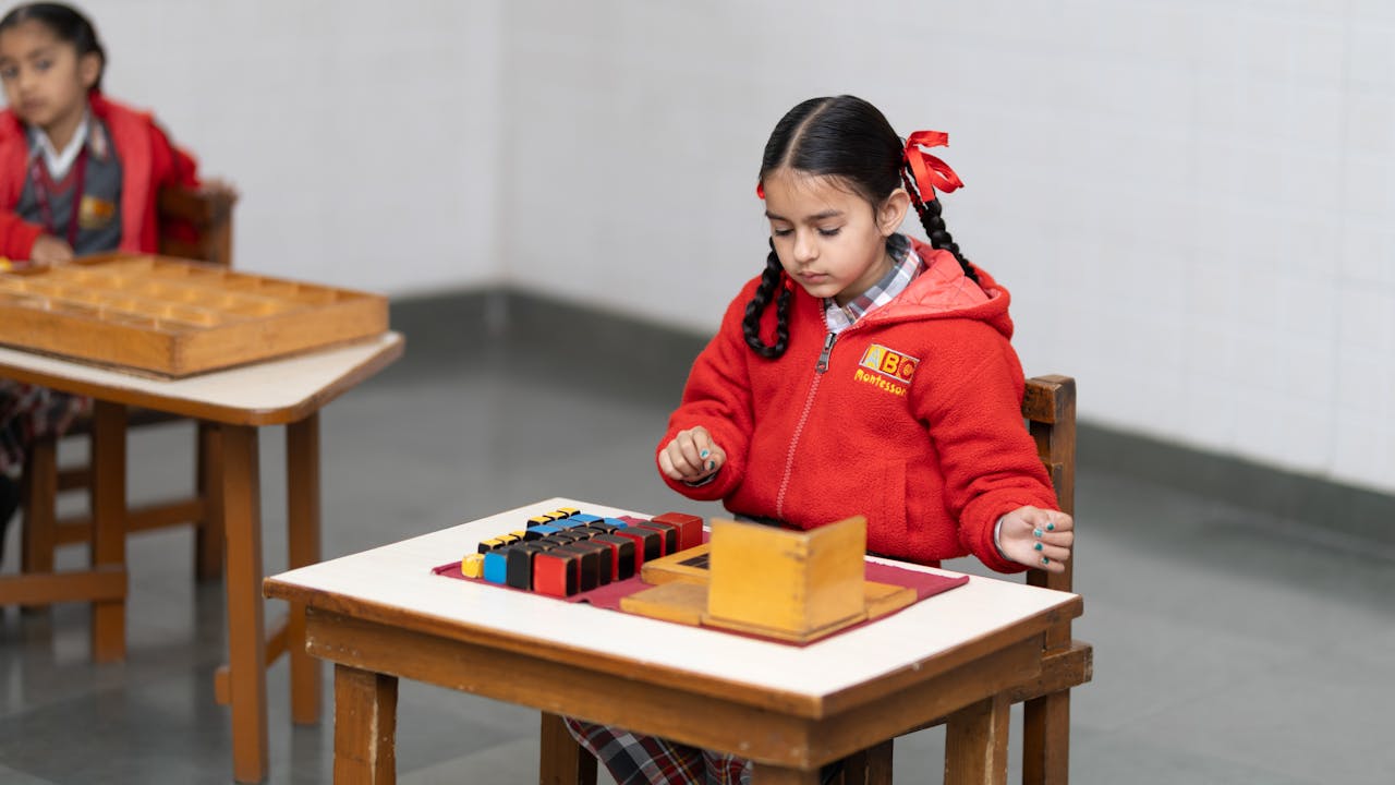 about-01 A young girl in a classroom focused on a Montessori educational activity with colorful blocks.